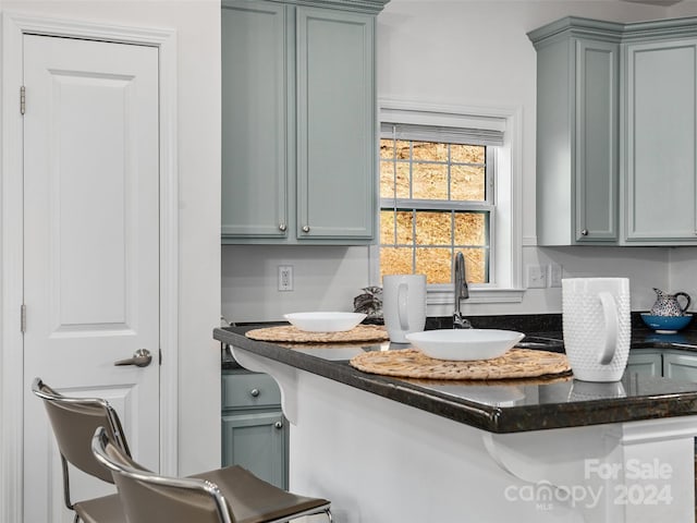 interior space with a breakfast bar, kitchen peninsula, sink, and dark stone counters