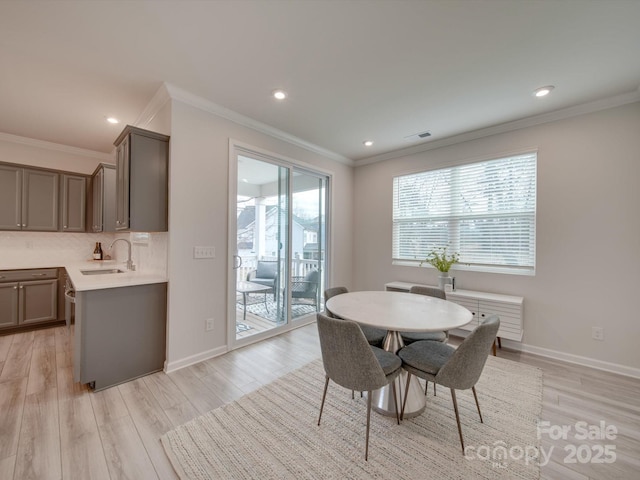 dining area with ornamental molding, sink, and light hardwood / wood-style flooring