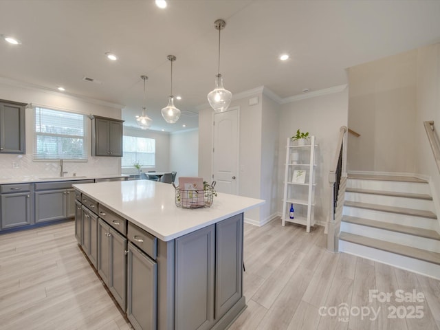 kitchen with gray cabinetry, sink, light hardwood / wood-style flooring, a kitchen island, and hanging light fixtures