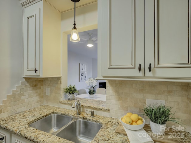 kitchen featuring backsplash, light stone counters, hanging light fixtures, and sink