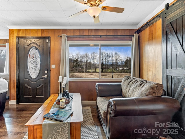 living room featuring a barn door, wood walls, ceiling fan, and ornamental molding