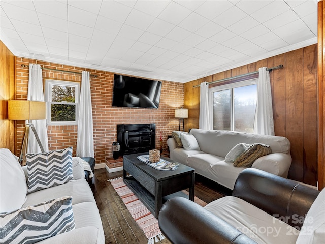 living room with a wood stove, dark wood-type flooring, brick wall, wooden walls, and ornamental molding