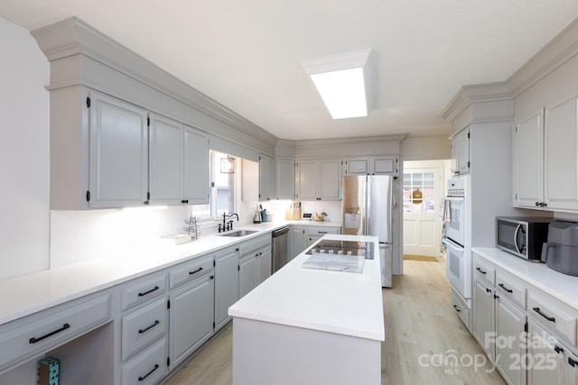 kitchen with appliances with stainless steel finishes, gray cabinetry, a kitchen island, light hardwood / wood-style flooring, and sink