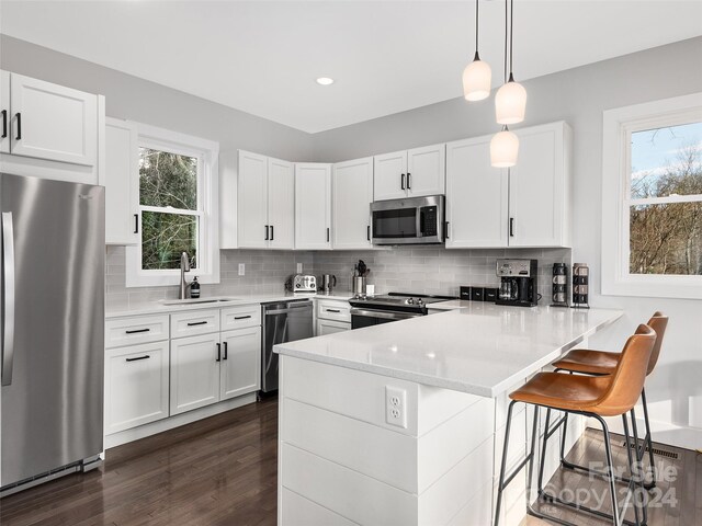 kitchen featuring kitchen peninsula, appliances with stainless steel finishes, a wealth of natural light, decorative light fixtures, and white cabinetry