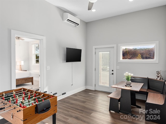 game room featuring dark hardwood / wood-style floors, ceiling fan, and a wall unit AC