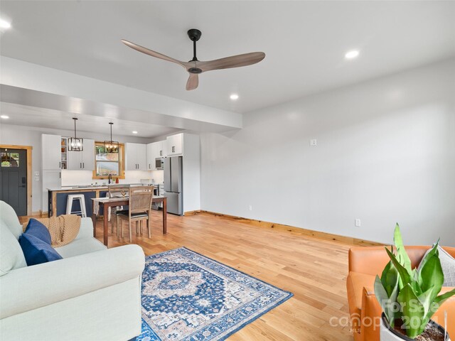 living room with ceiling fan with notable chandelier and light hardwood / wood-style flooring