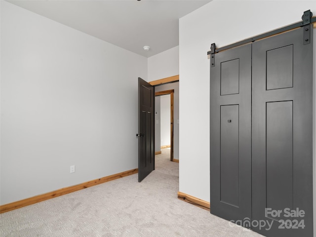 unfurnished bedroom with a barn door and light carpet