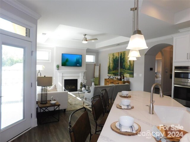 dining room with ceiling fan, sink, dark wood-type flooring, a raised ceiling, and ornamental molding