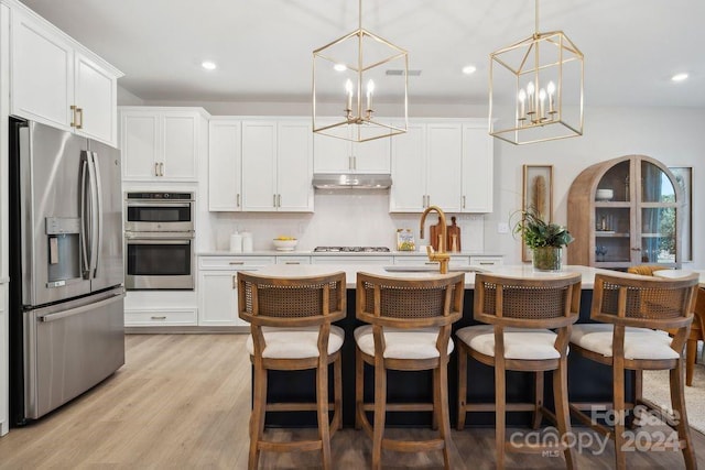 kitchen with appliances with stainless steel finishes, decorative light fixtures, white cabinetry, and an island with sink