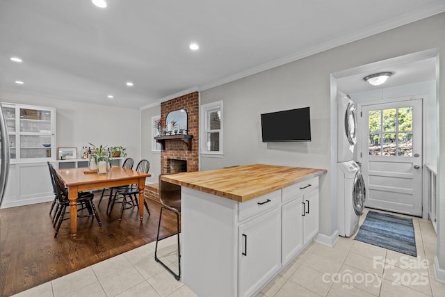 kitchen featuring wooden counters, white cabinetry, a kitchen breakfast bar, stacked washer and clothes dryer, and a brick fireplace