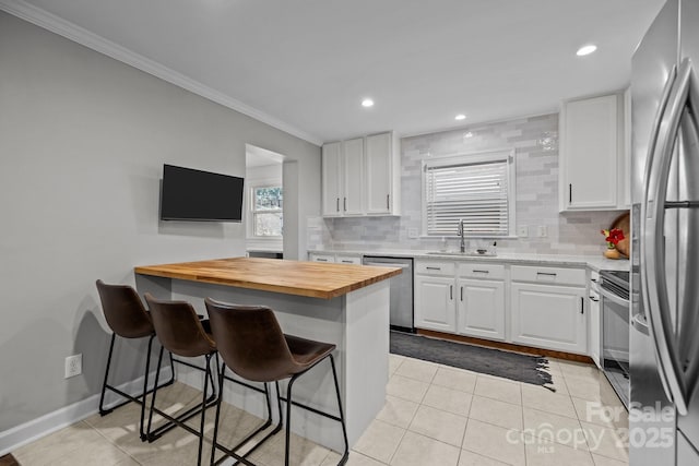 kitchen featuring a breakfast bar, butcher block countertops, white cabinetry, and stainless steel appliances