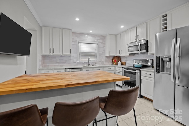 kitchen with wood counters, appliances with stainless steel finishes, sink, light tile patterned floors, and white cabinets