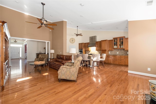 living room with ceiling fan, high vaulted ceiling, ornamental molding, and light wood-type flooring