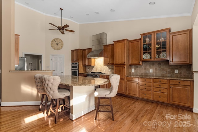 kitchen featuring crown molding, wall chimney exhaust hood, appliances with stainless steel finishes, tasteful backsplash, and a breakfast bar area