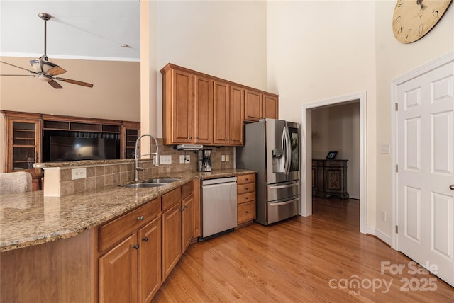 kitchen with sink, stainless steel appliances, light stone counters, a towering ceiling, and light hardwood / wood-style floors