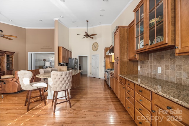 kitchen featuring light stone counters, crown molding, appliances with stainless steel finishes, exhaust hood, and light wood-type flooring