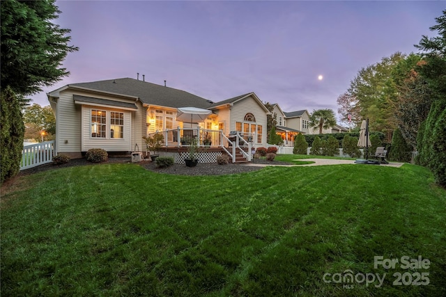 back house at dusk with a lawn and a wooden deck