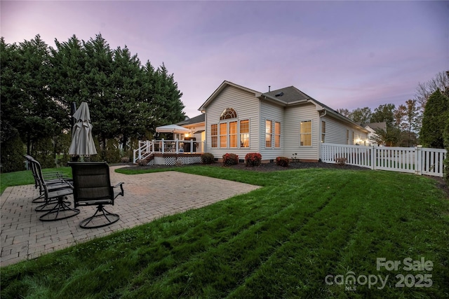 back house at dusk with a lawn, a patio area, and a deck