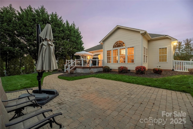 back house at dusk with a patio area, a yard, and a deck