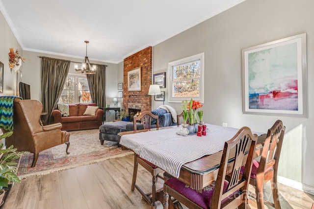 dining space with a fireplace, ornamental molding, light hardwood / wood-style floors, and a notable chandelier