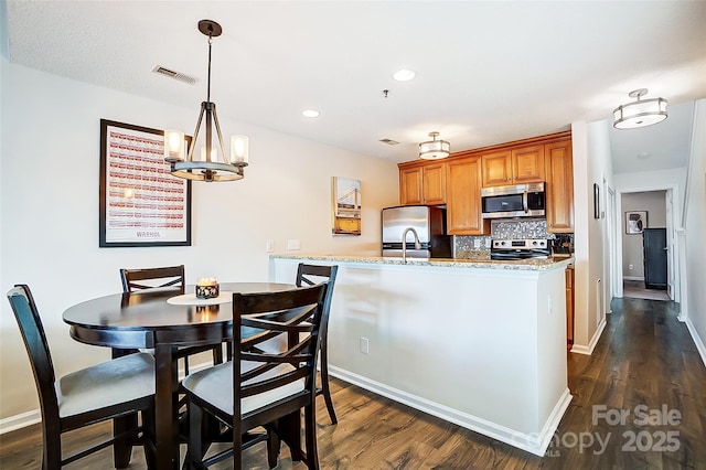 kitchen featuring stainless steel appliances, hanging light fixtures, dark wood-type flooring, and decorative backsplash