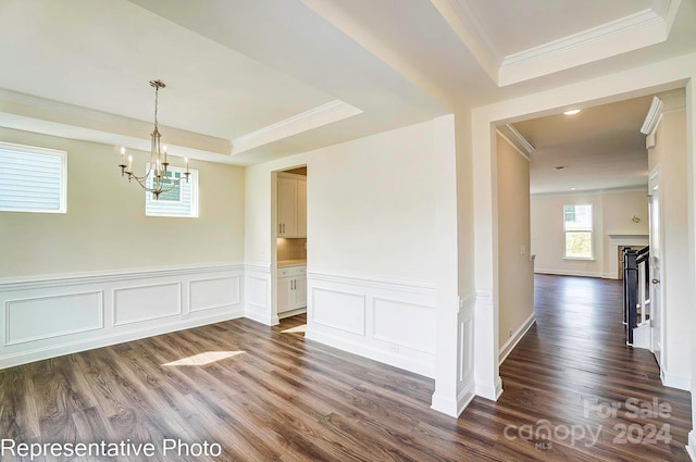 unfurnished dining area with a raised ceiling, dark hardwood / wood-style flooring, an inviting chandelier, and crown molding