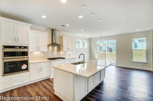 kitchen with a kitchen island with sink, sink, wall chimney exhaust hood, appliances with stainless steel finishes, and white cabinetry