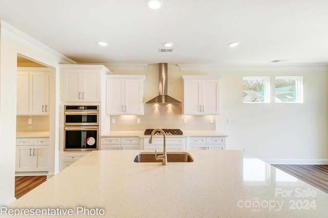 kitchen with wall chimney range hood, sink, tasteful backsplash, white cabinetry, and stainless steel appliances