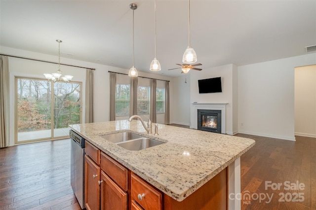 kitchen with dark wood-type flooring, a sink, stainless steel dishwasher, brown cabinets, and a glass covered fireplace