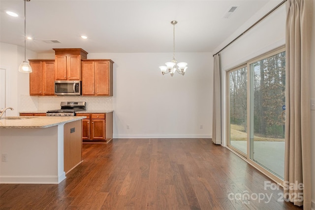 kitchen featuring appliances with stainless steel finishes, brown cabinetry, a sink, and tasteful backsplash