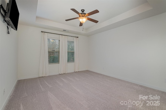 carpeted spare room with ceiling fan, a tray ceiling, visible vents, and baseboards