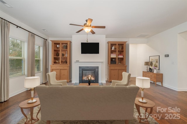 living room with a ceiling fan, a glass covered fireplace, visible vents, and wood finished floors