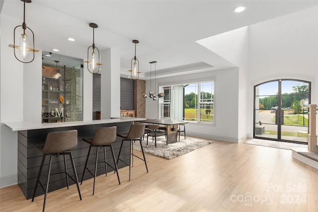 bar featuring pendant lighting, an inviting chandelier, a tray ceiling, and light hardwood / wood-style flooring