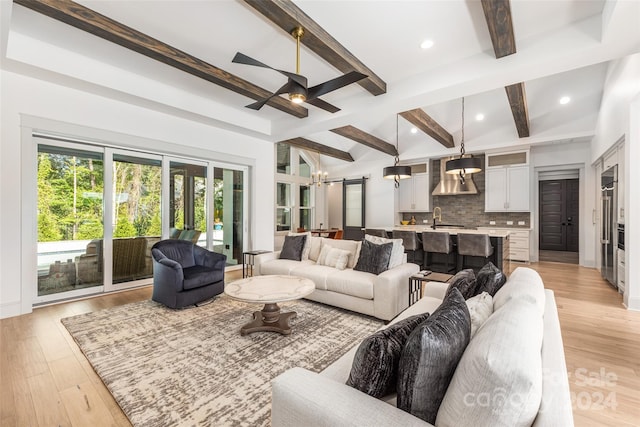 living room featuring vaulted ceiling with beams, ceiling fan with notable chandelier, light hardwood / wood-style floors, and sink