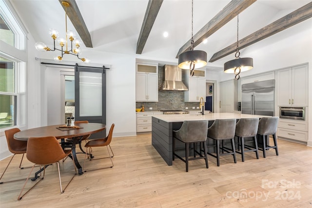 kitchen featuring wall chimney exhaust hood, a barn door, decorative light fixtures, white cabinets, and light hardwood / wood-style floors