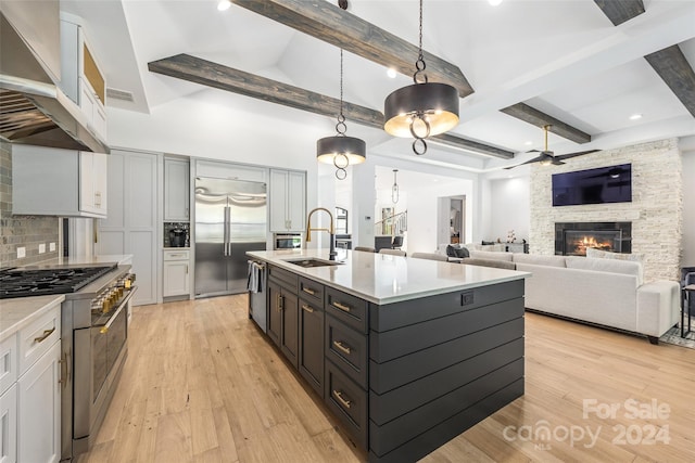 kitchen with extractor fan, high end appliances, a kitchen island with sink, sink, and decorative light fixtures