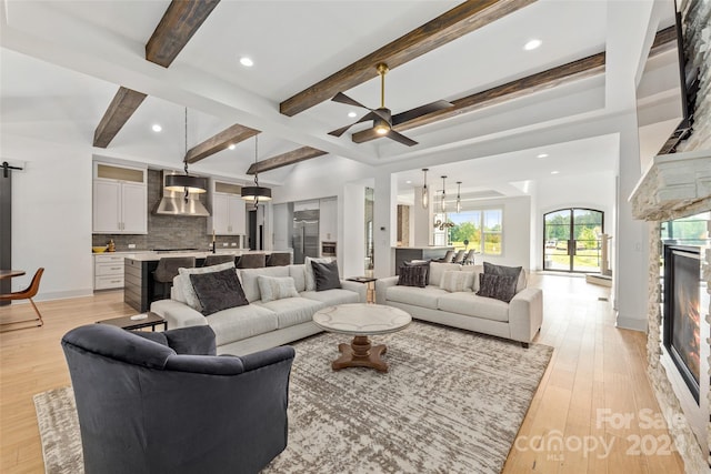 living room with a fireplace, ceiling fan, light hardwood / wood-style flooring, and beamed ceiling