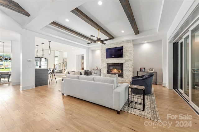 living room with beamed ceiling, ceiling fan, light wood-type flooring, and a fireplace