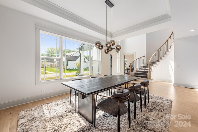 dining area featuring a raised ceiling, crown molding, light hardwood / wood-style flooring, and a chandelier