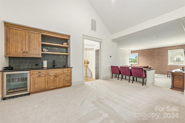 bar with light carpet, backsplash, sink, high vaulted ceiling, and wine cooler