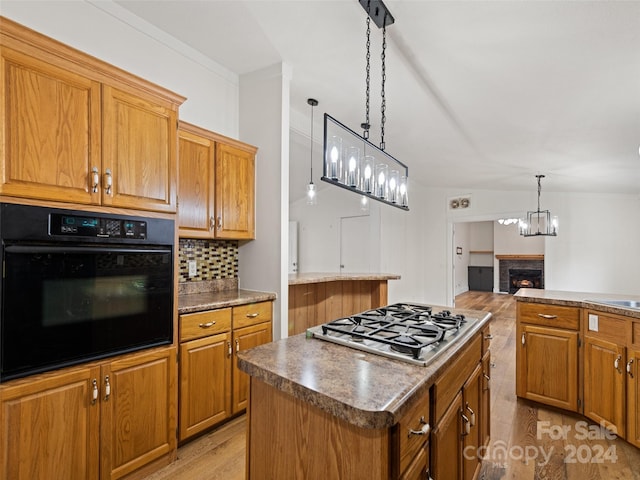 kitchen featuring stainless steel gas stovetop, black oven, a fireplace, a kitchen island, and light wood-type flooring