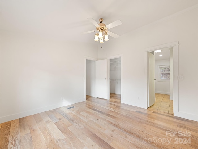 unfurnished bedroom with a closet, a walk in closet, ceiling fan, and light hardwood / wood-style flooring