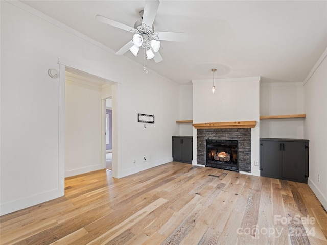 unfurnished living room with light wood-type flooring, a stone fireplace, ceiling fan, and crown molding