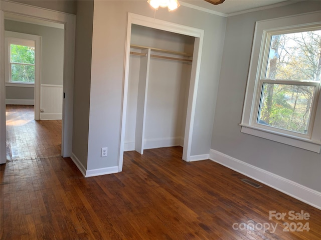 unfurnished bedroom featuring a closet, crown molding, dark wood-type flooring, and multiple windows