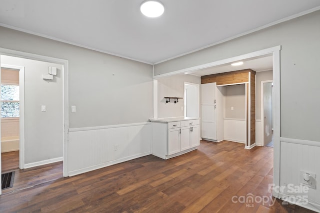 empty room featuring crown molding, dark wood-style floors, a wainscoted wall, and visible vents