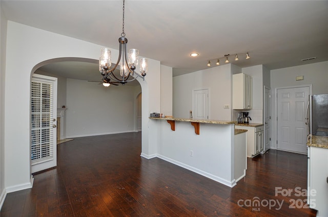 kitchen featuring decorative light fixtures, white cabinetry, stainless steel fridge, a kitchen breakfast bar, and kitchen peninsula