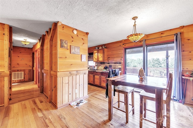 dining space with a textured ceiling, light hardwood / wood-style flooring, and wooden walls