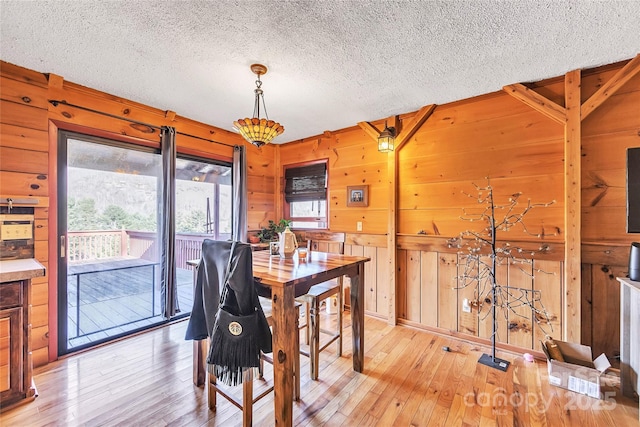 dining area with wooden walls, light hardwood / wood-style floors, and a textured ceiling