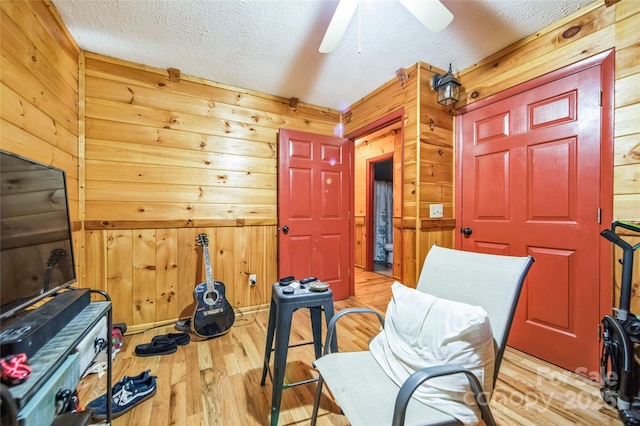 living area with ceiling fan, wood walls, a textured ceiling, and light hardwood / wood-style flooring