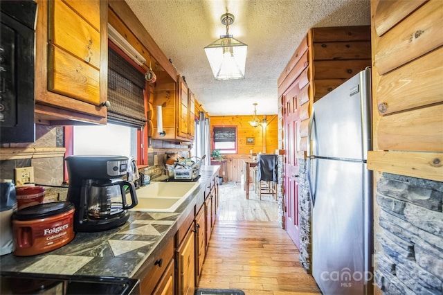 kitchen featuring wood walls, a textured ceiling, decorative light fixtures, light hardwood / wood-style floors, and stainless steel refrigerator